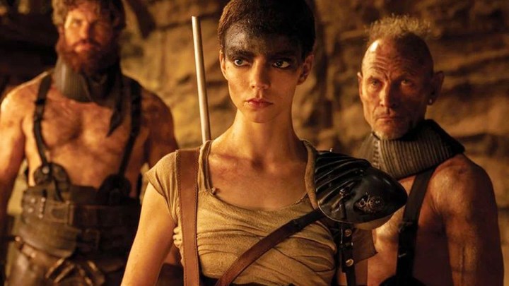 A woman stands with two men in Furiosa.